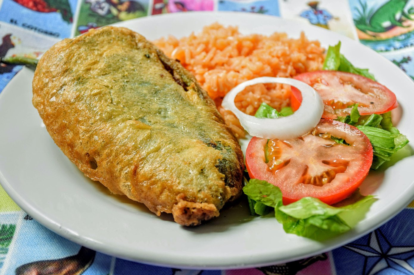 Mexican Chile Relleno (Poblano Chili Pepper) stuffed with groud beef meat and served with red rice and salad over a loteria carpet